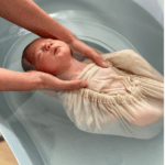 bébé dans un lilititi maintenu par les omoplates lors d'un rituel du bain sensoriel