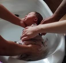 4 bras tenant un bébé mis sur le côté dans une baignoire bébé pour un rituel du bain sensoriel