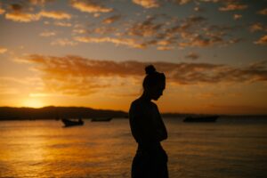 ombre d'une femme devant un coucher de soleil sur l'eau, quelques nuages dans le ciel